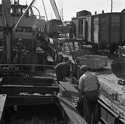 Lastfartyg vid kajkant lastas med lådor från järnvägsvagn.
