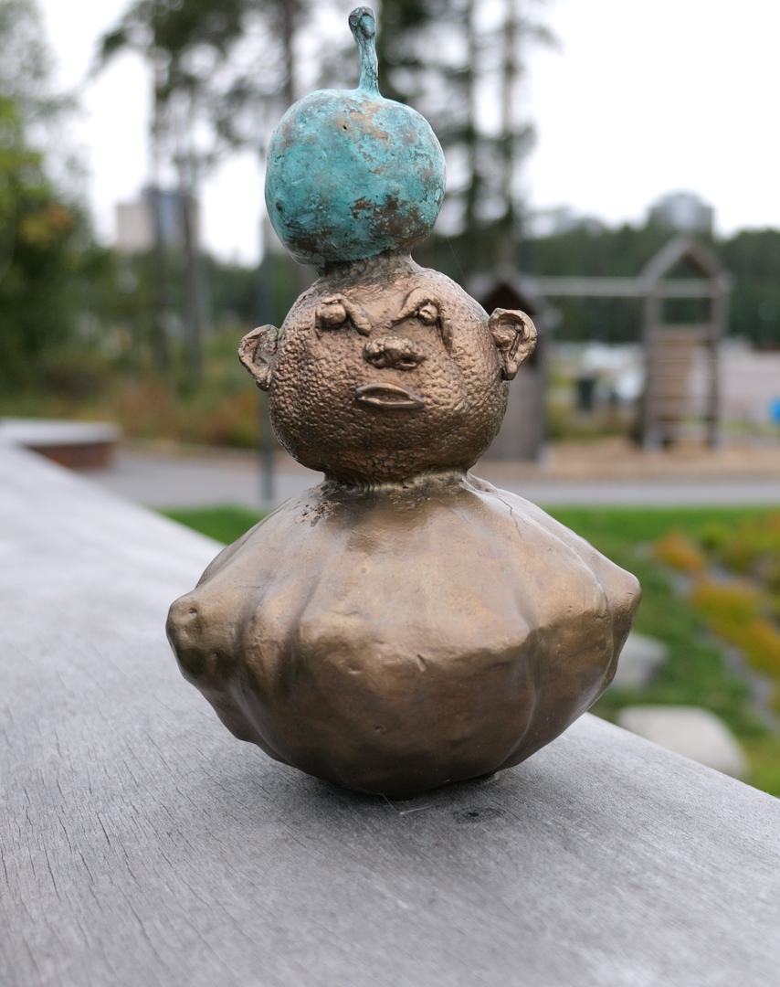 En liten bronsskulptur med huvud skulpterat efter en limefrukt och kroppen efter en pumpa.