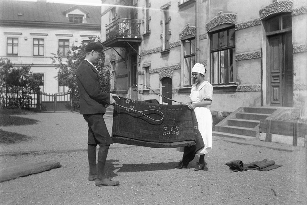 Gustav och hembiträdet Gunhild piskar matta på innergården.