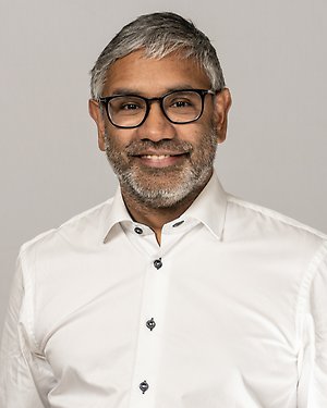 Fredrik Hansson ler mot kameran. Han bär en vit skjorta och svarta glasögon.