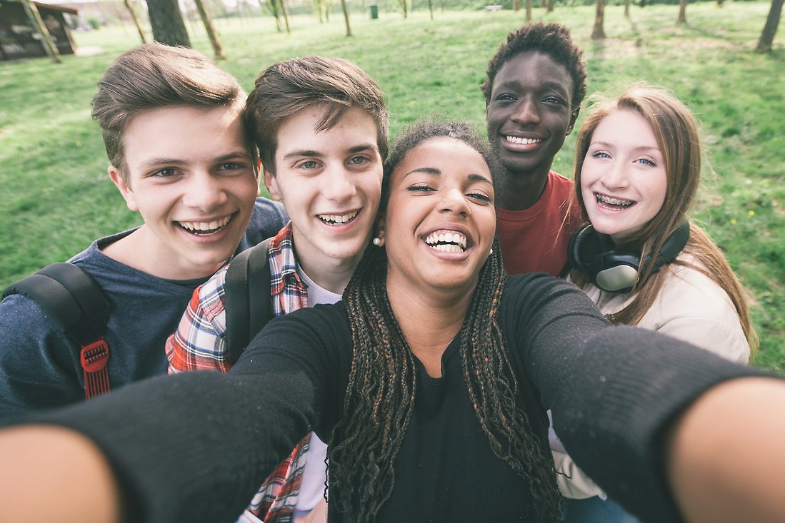 Glada ungdomar tar en gruppbild med grönska i bakgrunden