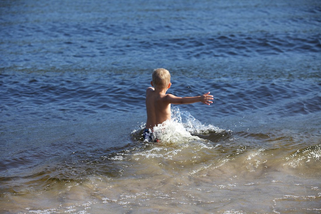 Ett barn som badar vid ett friluftsbad och plaskar i vattnet